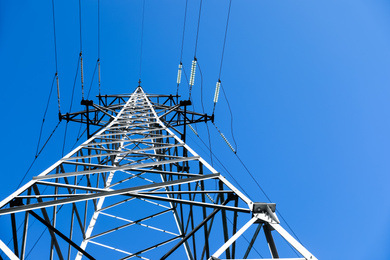 Modern high voltage tower against blue sky, low angle view