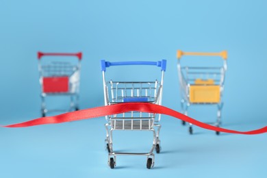 Photo of Shopping cart at red finish line on light blue background. Competition concept