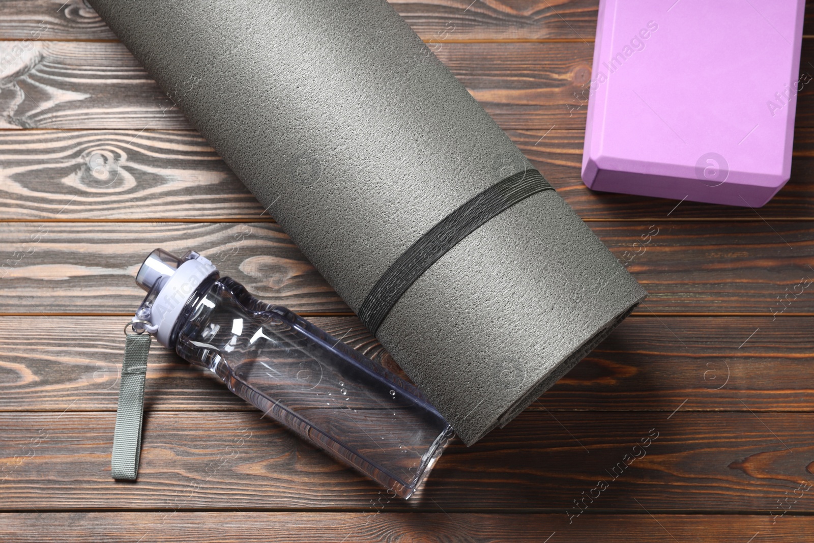 Photo of Exercise mat, yoga block and bottle of water on wooden floor, flat lay