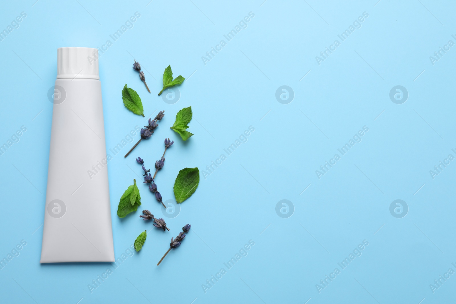 Photo of Blank tube of toothpaste with mint and lavender flowers on turquoise background, flat lay. Space for text