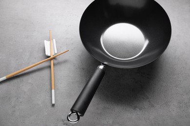 Empty iron wok and wooden chopsticks on grey table