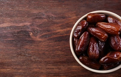 Sweet dried dates in bowl on wooden background, top view. Space for text