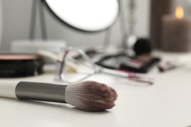 Makeup brush and cosmetic products on dressing table, closeup