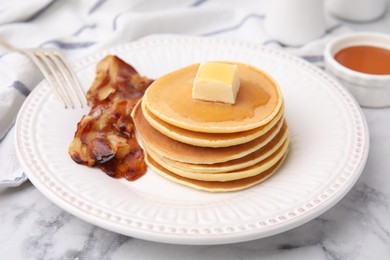 Photo of Delicious pancakes with butter, maple syrup and fried bacon on white marble table