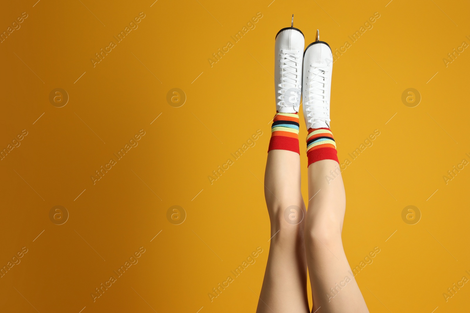 Photo of Woman in elegant white ice skates on yellow background, closeup of legs. Space for text