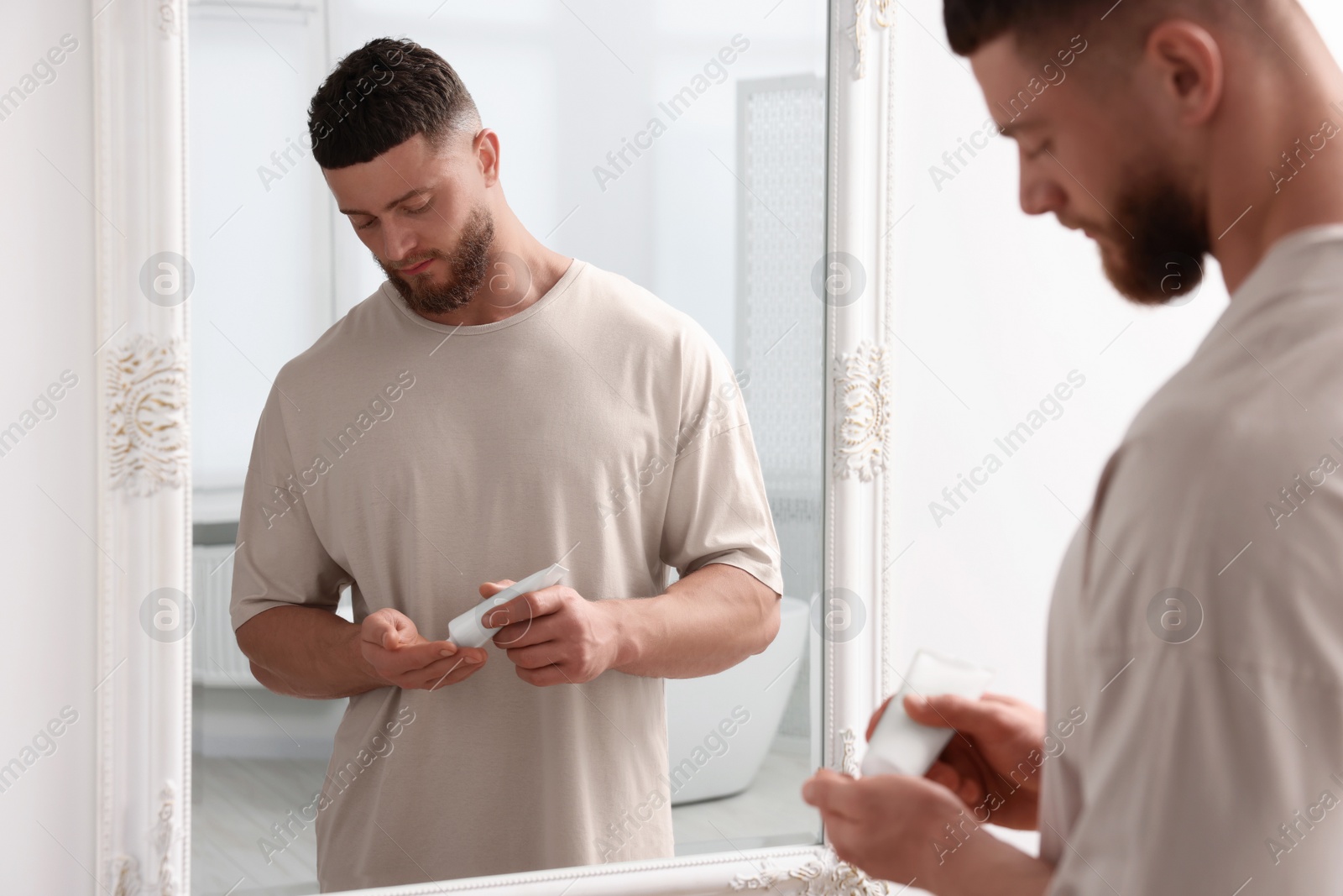 Photo of Handsome man applying body cream near mirror in bathroom