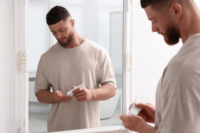 Photo of Handsome man applying body cream near mirror in bathroom