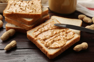 Photo of Delicious toasts with peanut butter, nuts and knife on dark wooden table, closeup