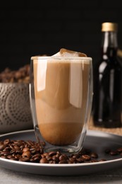 Glass of aromatic coffee with syrup and beans on light grey table