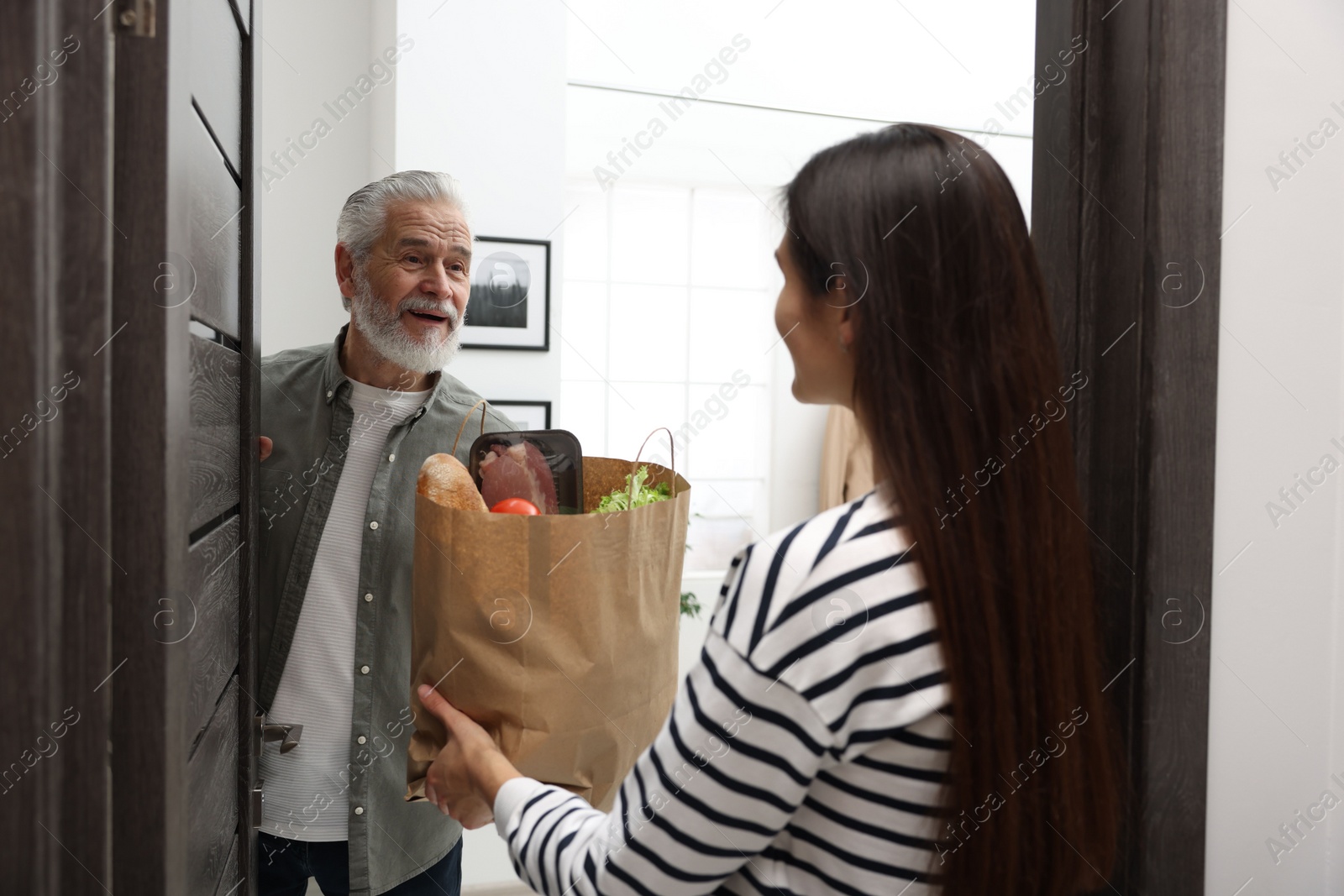 Photo of Courier giving paper bag with food products to senior man indoors