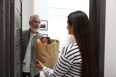 Photo of Courier giving paper bag with food products to senior man indoors