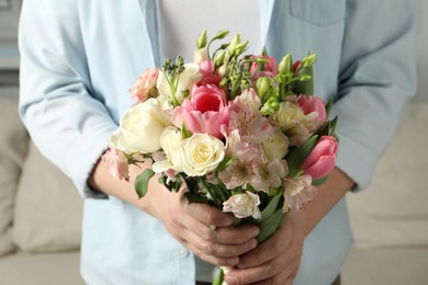 Photo of Man holding bouquet of beautiful flowers indoors, closeup