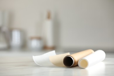 Photo of Rolls of baking paper on white marble table against blurred background indoors. Space for text