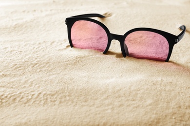 Stylish sunglasses on white sand. Space for text