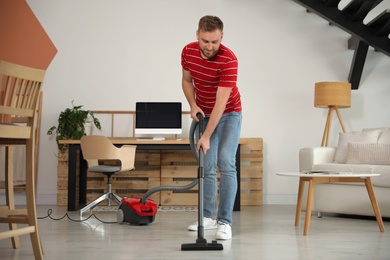 Young man using vacuum cleaner at home