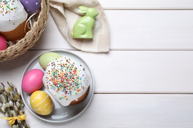 Flat lay composition with Easter cakes and color eggs on white wooden table, space for text