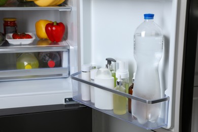 Photo of Storage of cosmetics and water in refrigerator door bin next to groceries