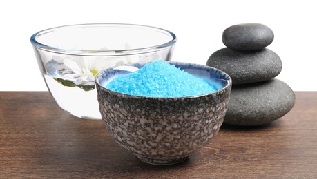 Photo of Light blue sea salt in bowl, spa stones and flowers on wooden table against white background
