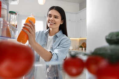 Photo of Young woman taking bottle of juice out of refrigerator in kitchen, view from inside