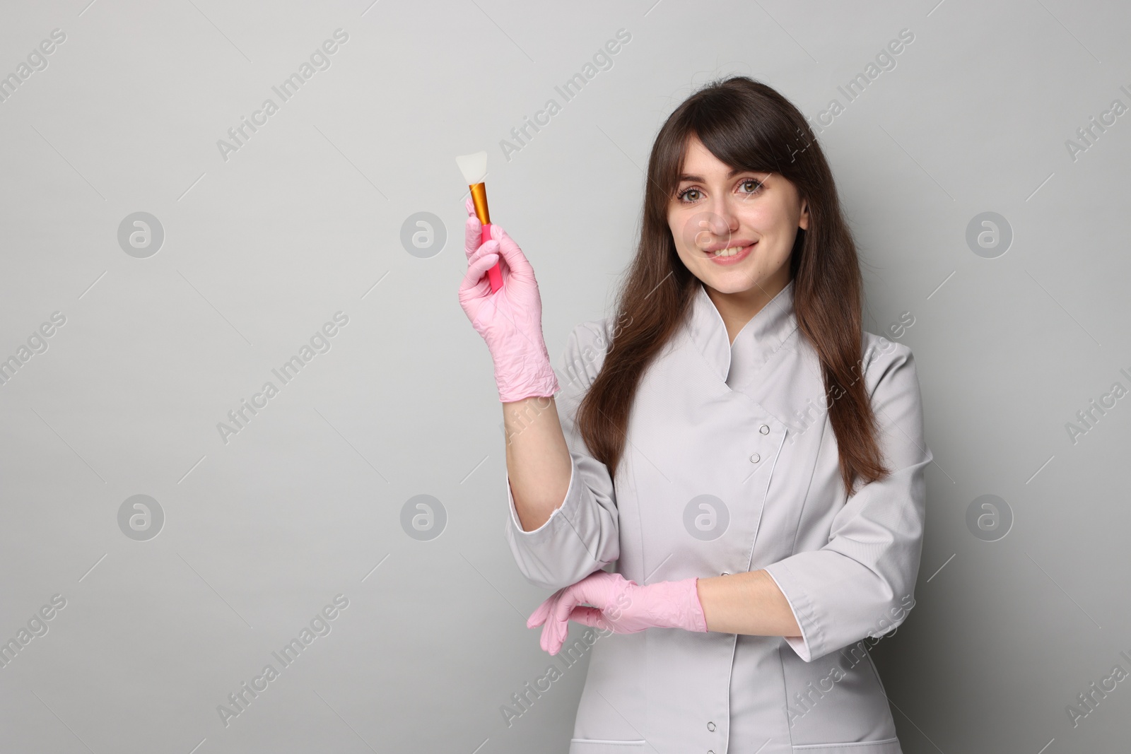 Photo of Cosmetologist with silicone cosmetic brush on grey background, space for text