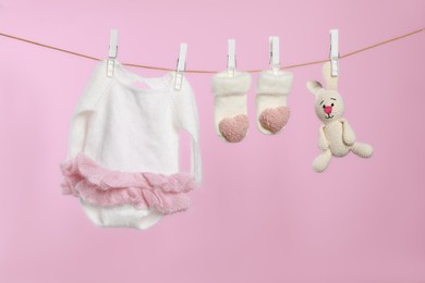 Photo of Baby clothes and handmade toy drying on washing line against pink background
