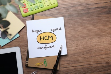 Paper with HCM abbreviation and space for text on wooden office table, flat lay. Human Capital Management