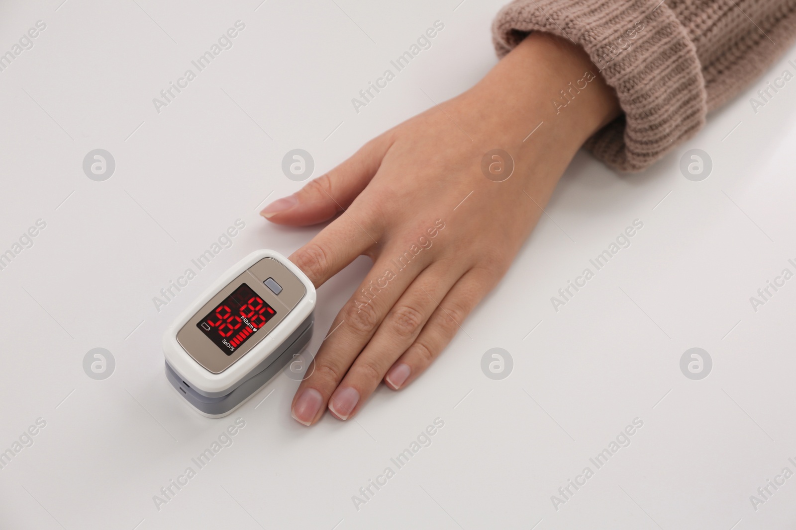 Photo of Woman measuring oxygen level with modern fingertip pulse oximeter at white table, top view