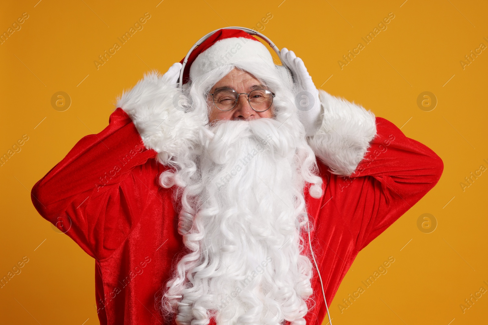 Photo of Merry Christmas. Santa Claus with headphones listening to music on orange background