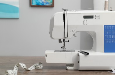 Photo of White sewing machine and measuring tape on wooden table indoors