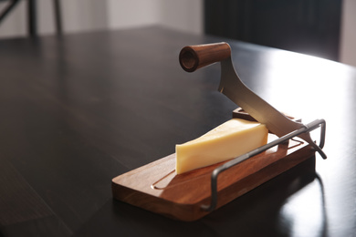 Photo of Slicer and piece of cheese on table. Space for text