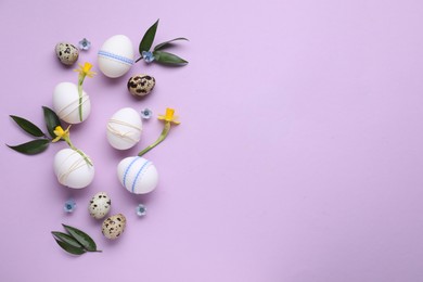 Photo of Festively decorated Easter eggs and green leaves on lilac background, flat lay. Space for text