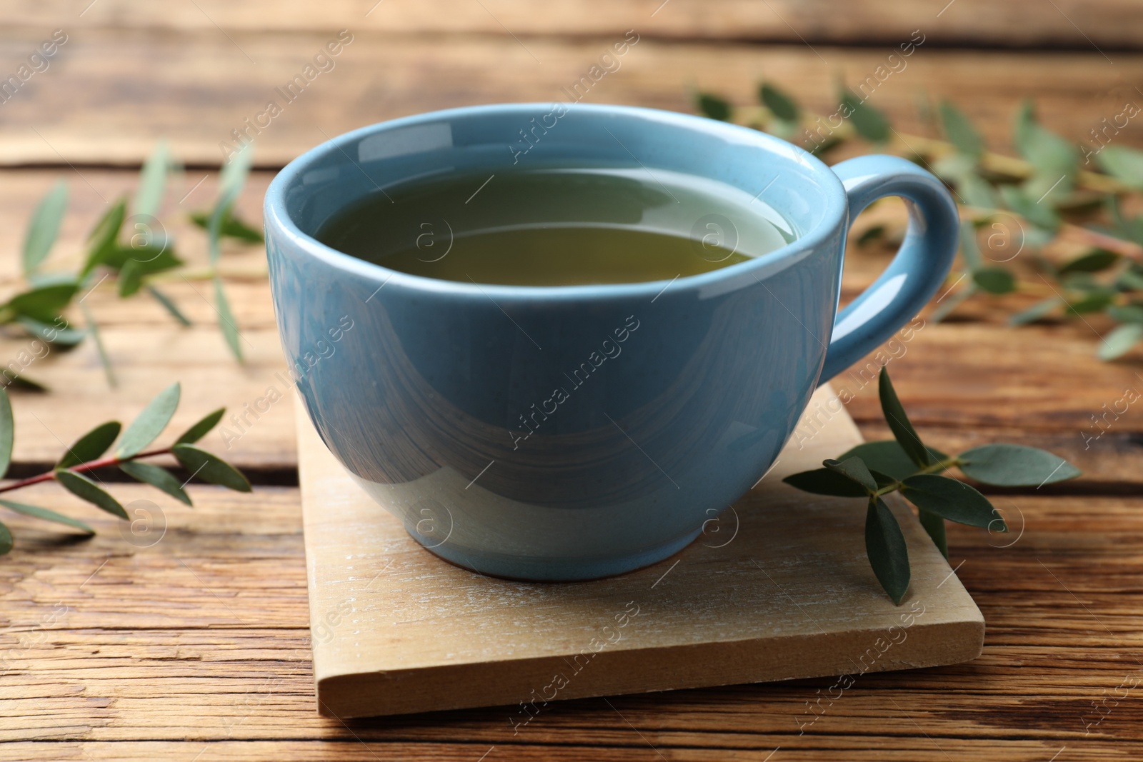 Photo of Cup of green tea and eucalyptus leaves on wooden table