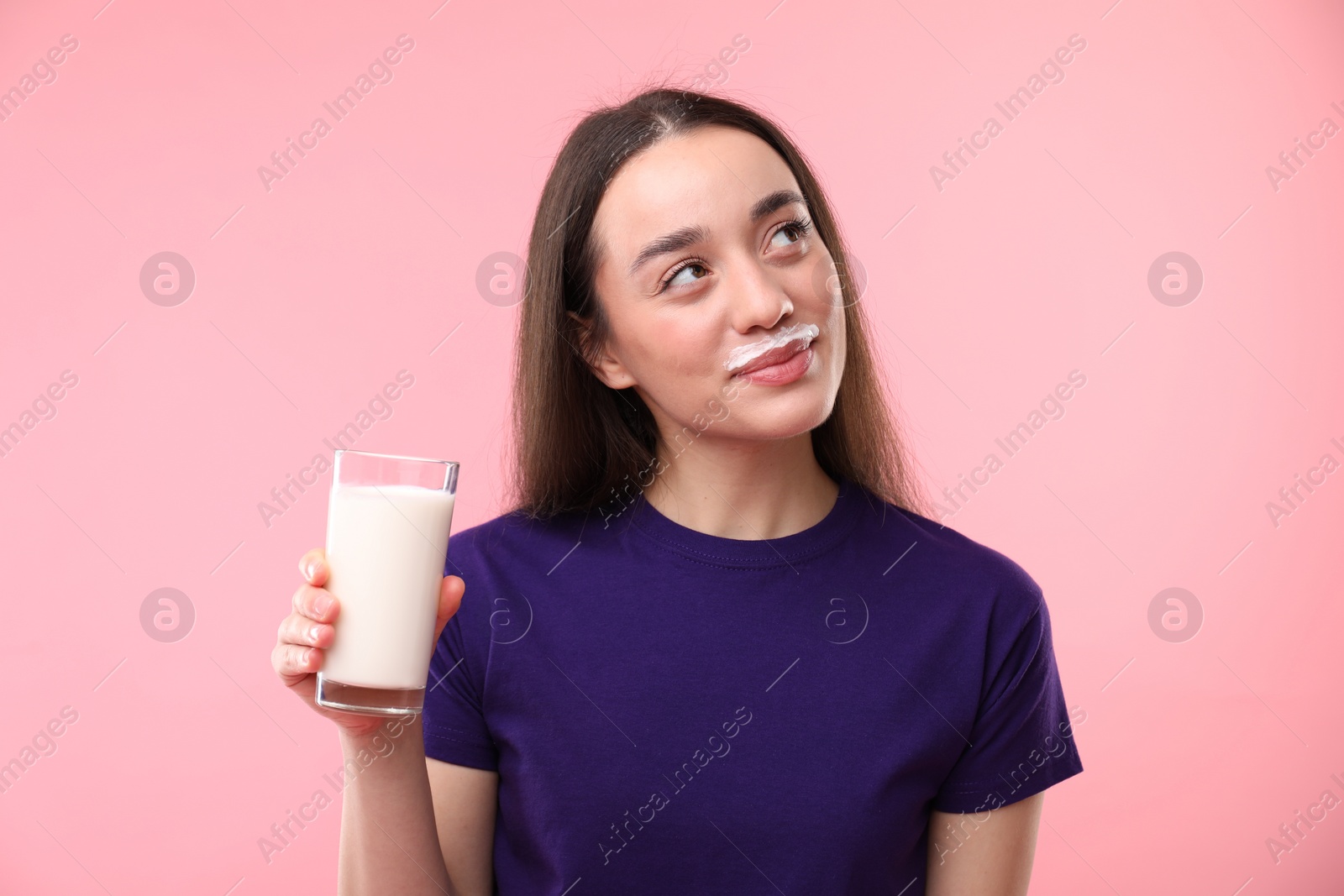 Photo of Cute woman with milk mustache holding glass of tasty dairy drink on pink background