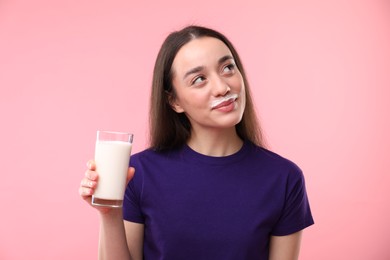 Photo of Cute woman with milk mustache holding glass of tasty dairy drink on pink background