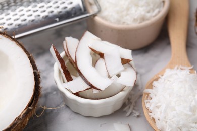 Photo of Coconut flakes, pieces, spoon and grater on white marble table