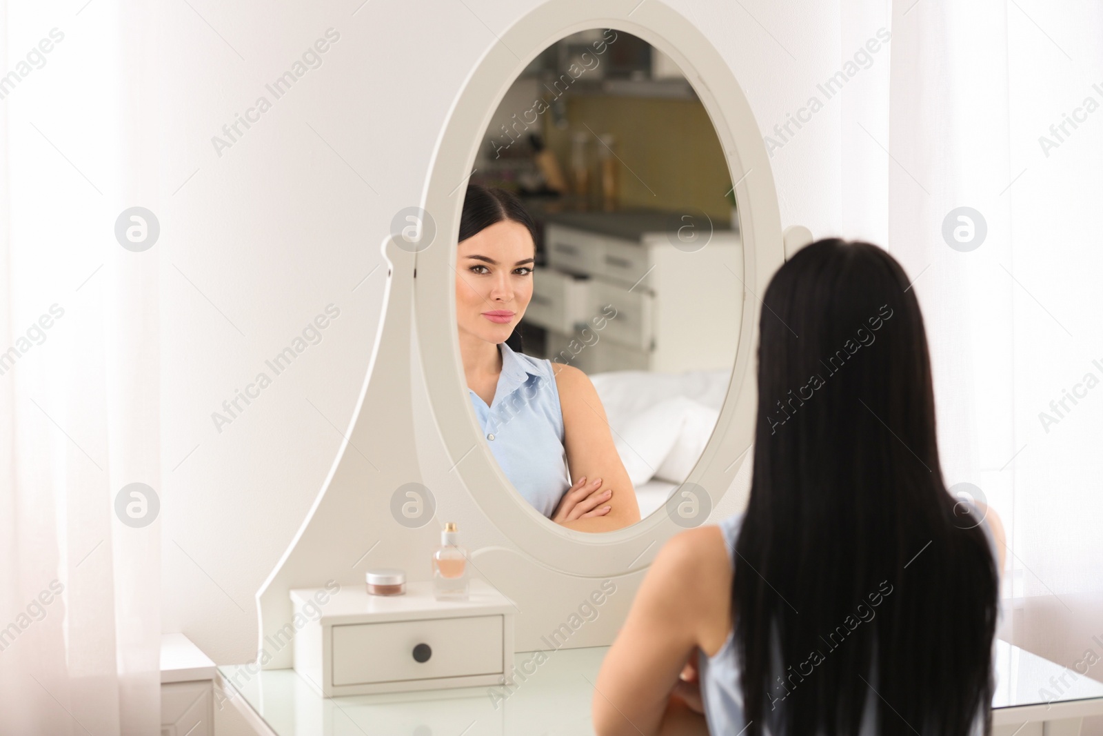 Photo of Beautiful young woman looking at herself in mirror indoors