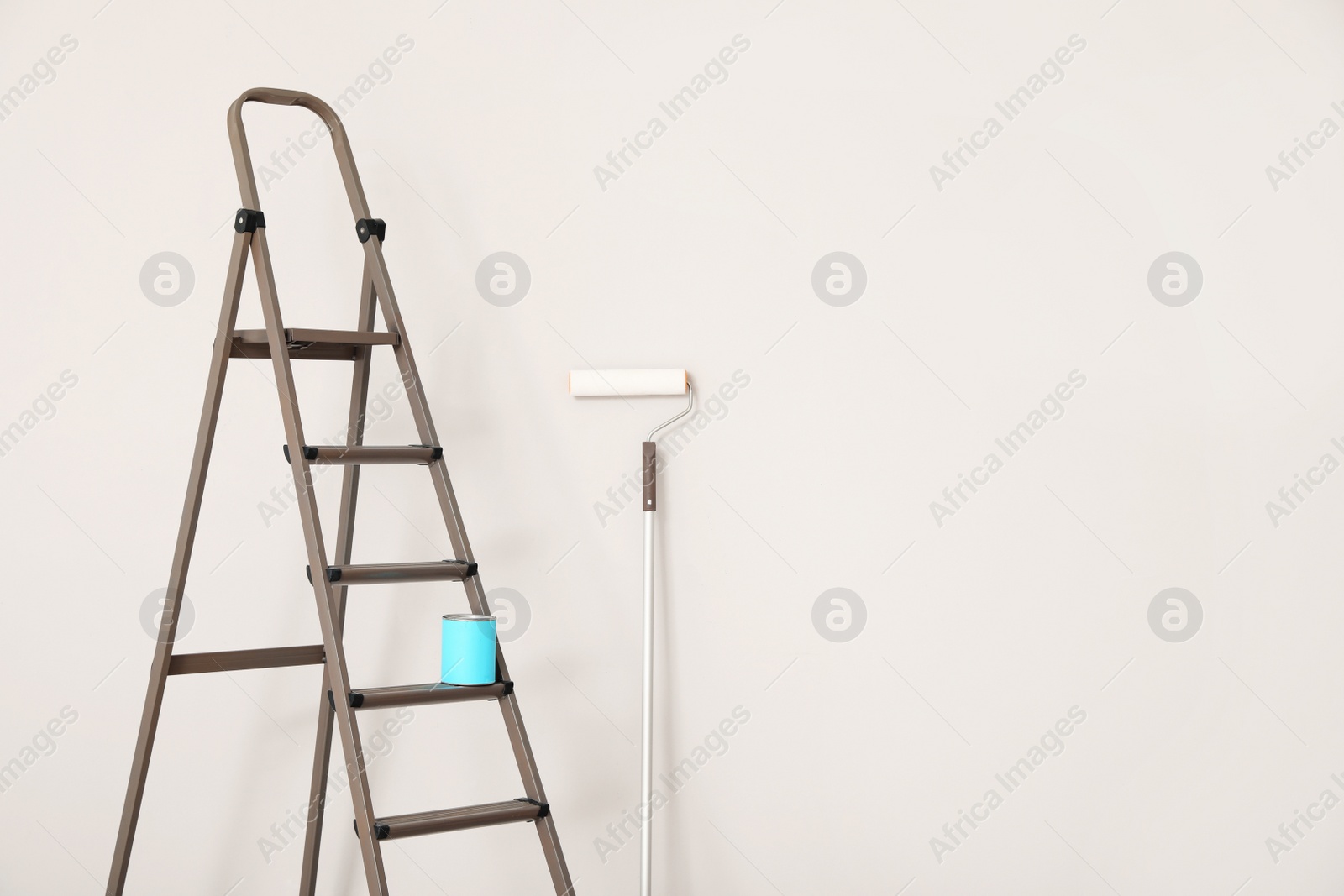 Photo of Can of paint on ladder and roller near white wall indoors, space for text