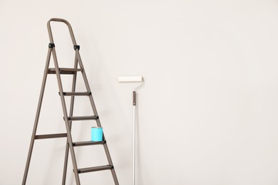 Photo of Can of paint on ladder and roller near white wall indoors, space for text
