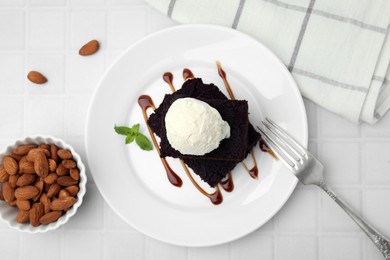 Tasty brownies served with ice cream and caramel sauce on white tiled table, flat lay
