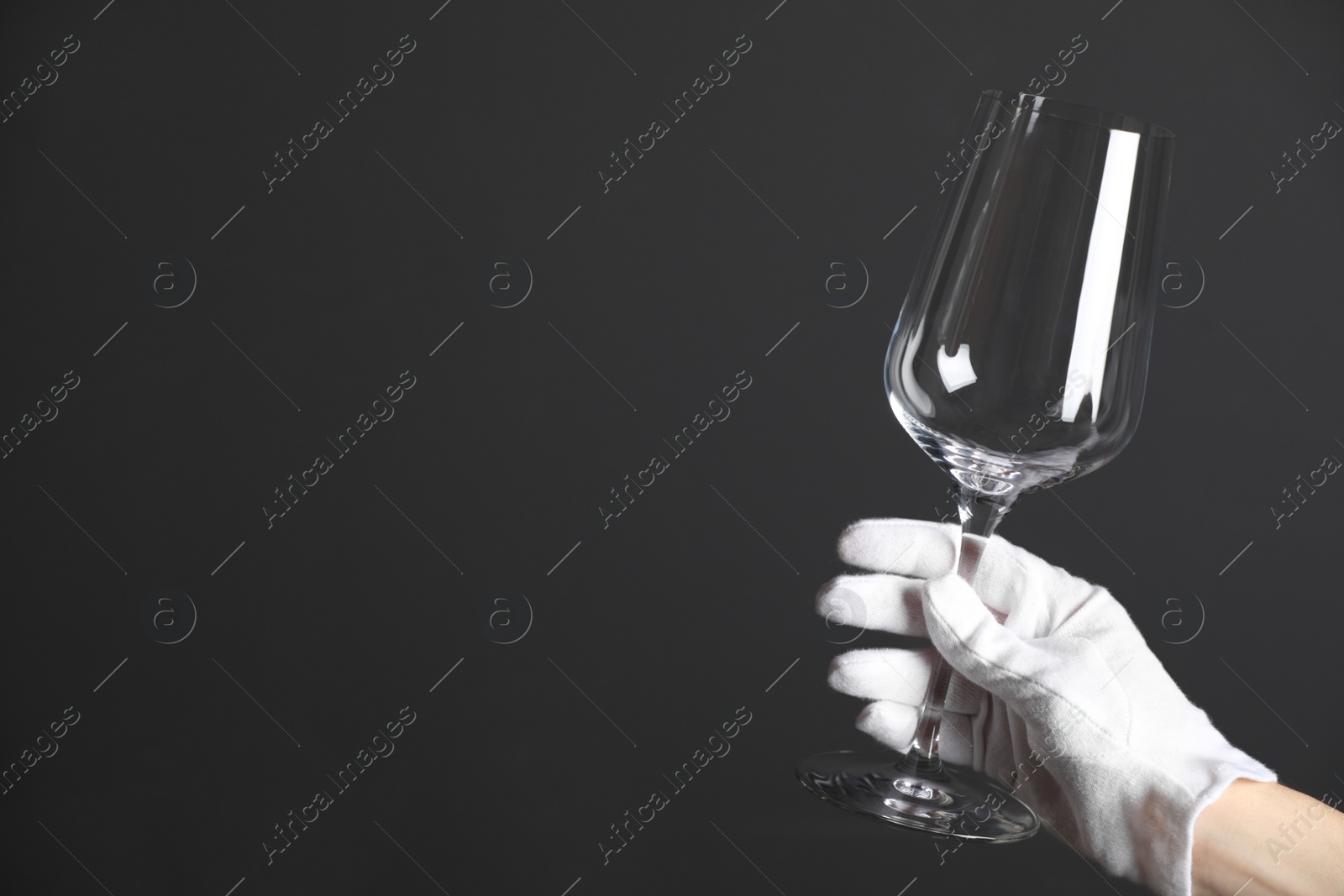 Photo of Person in white glove checking cleanliness of glass on dark background, closeup. Space for text