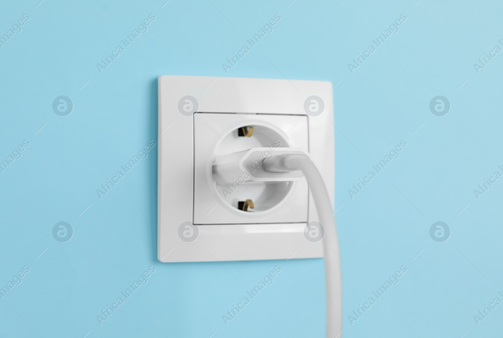 Photo of Charger adapter plugged into power socket on light blue wall. Electrical supply