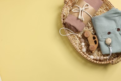 Photo of Different baby accessories and clothes in wicker basket on yellow background, top view