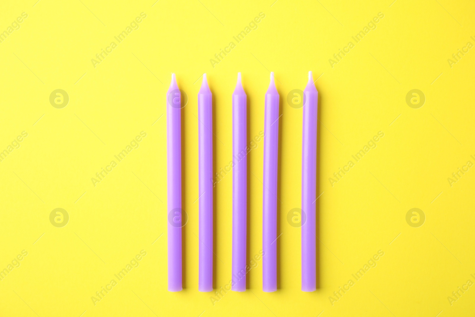 Photo of Purple birthday candles on yellow background, top view