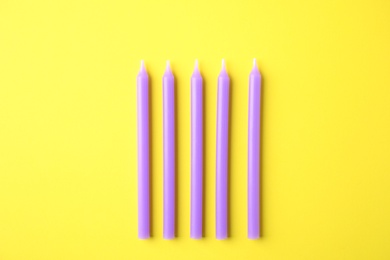 Photo of Purple birthday candles on yellow background, top view