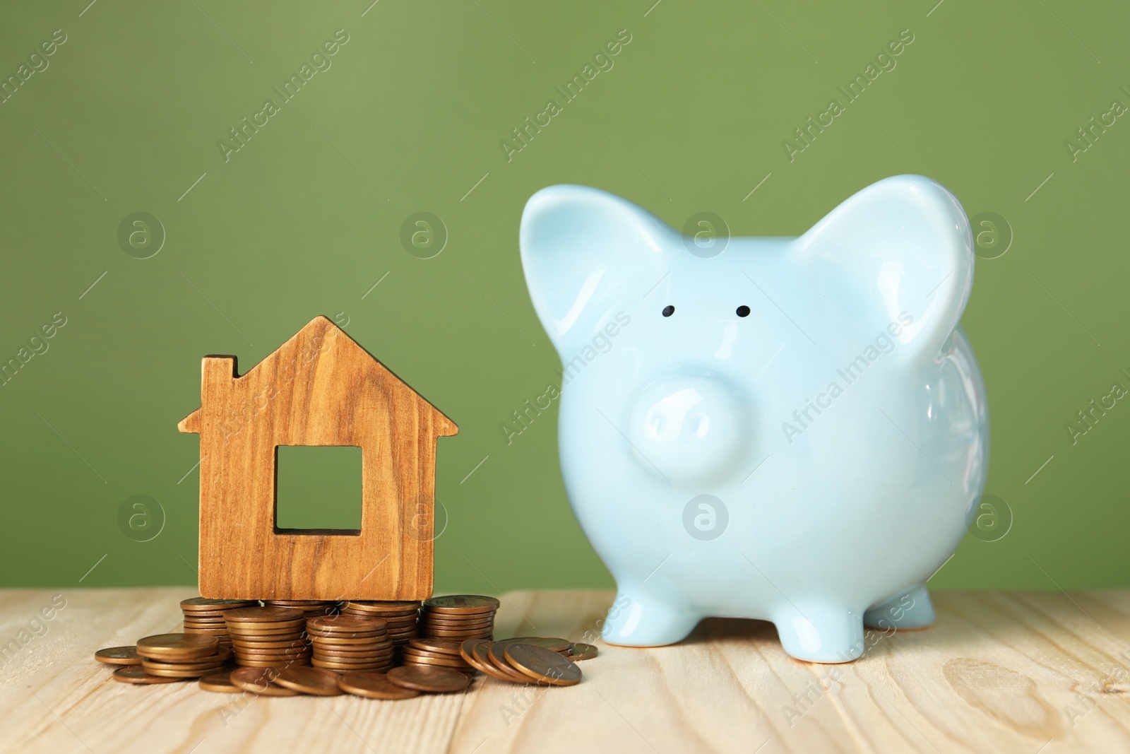 Photo of House model, coins and piggy bank on wooden table against green background