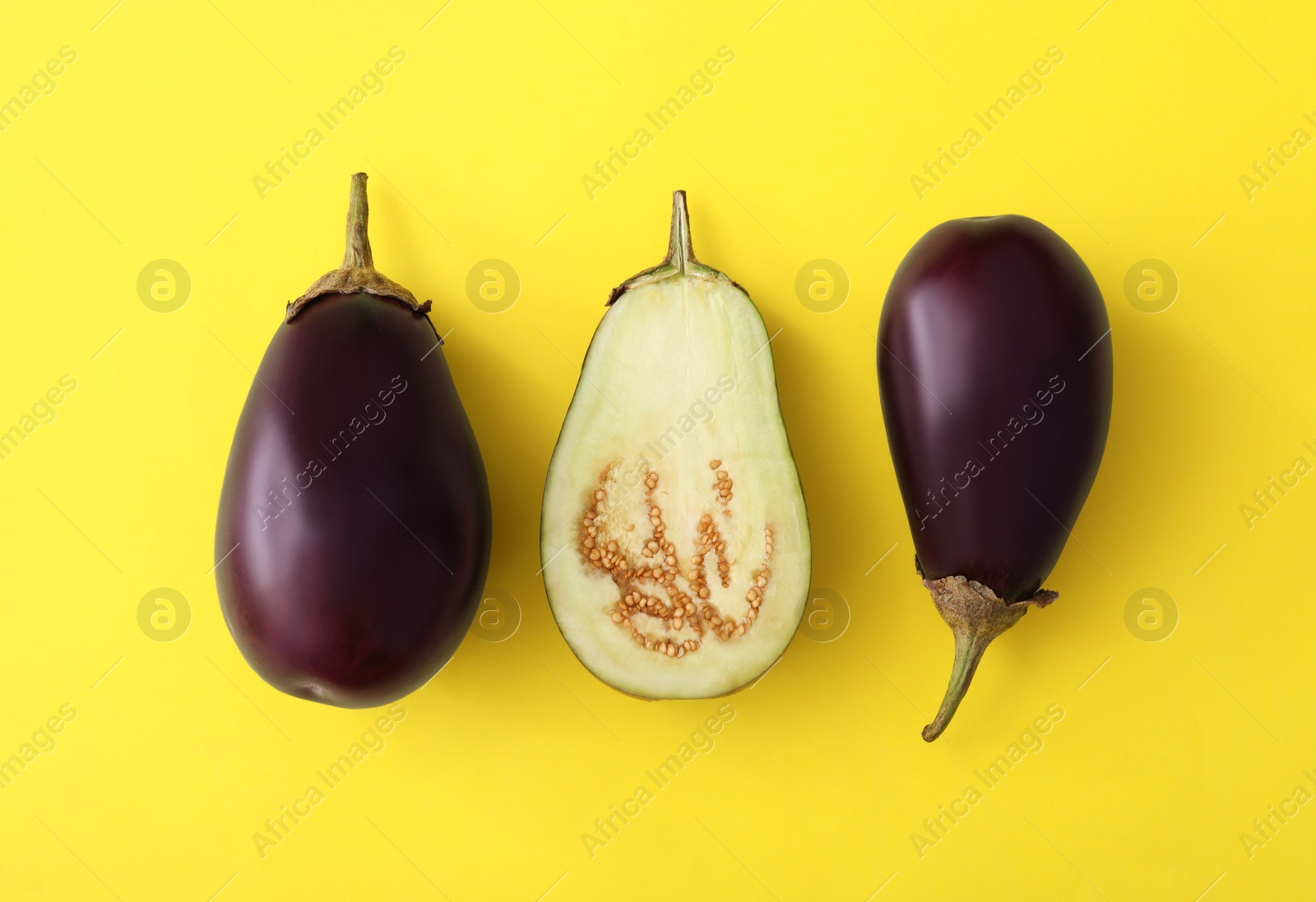 Photo of Cut and whole raw ripe eggplants on yellow background, flat lay