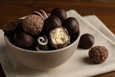 Photo of Bowl with many different delicious chocolate truffles on wooden table