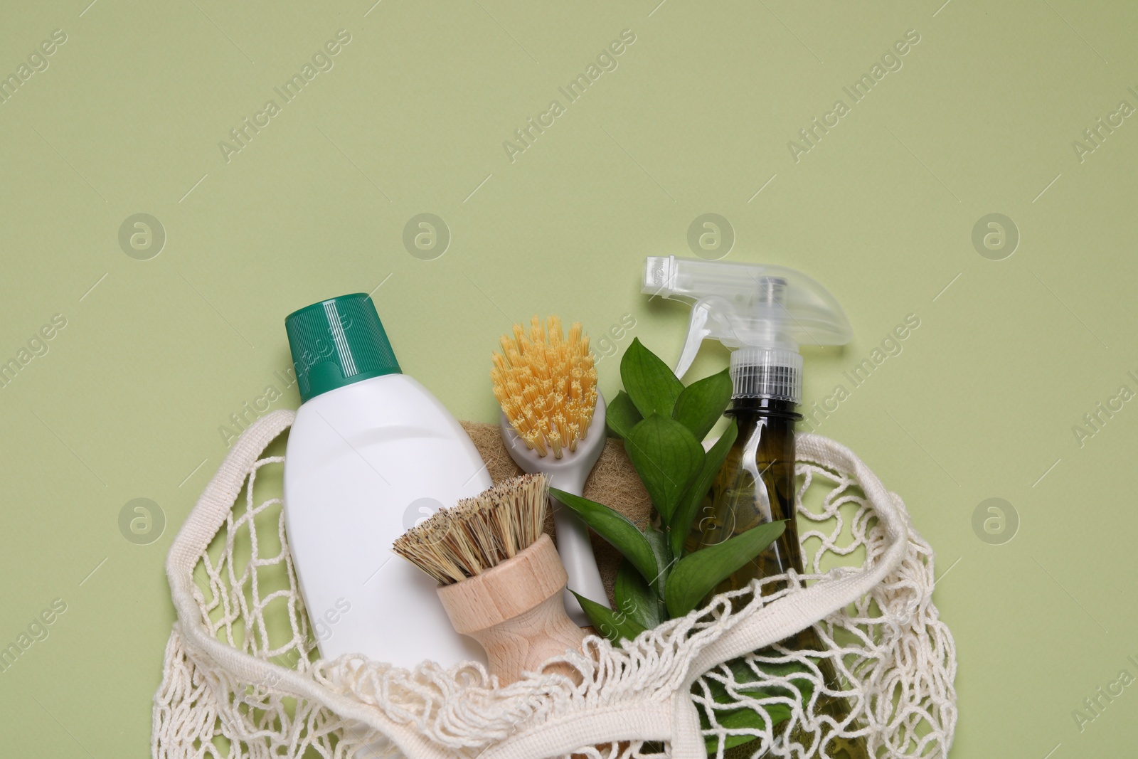 Photo of Different cleaning supplies in string bag on green background, space for text