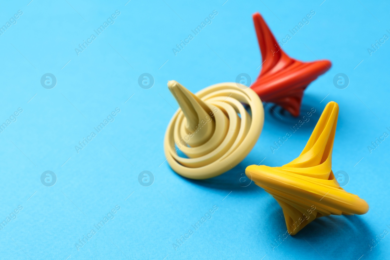 Photo of Many colorful spinning tops on light blue background, closeup. Space for text