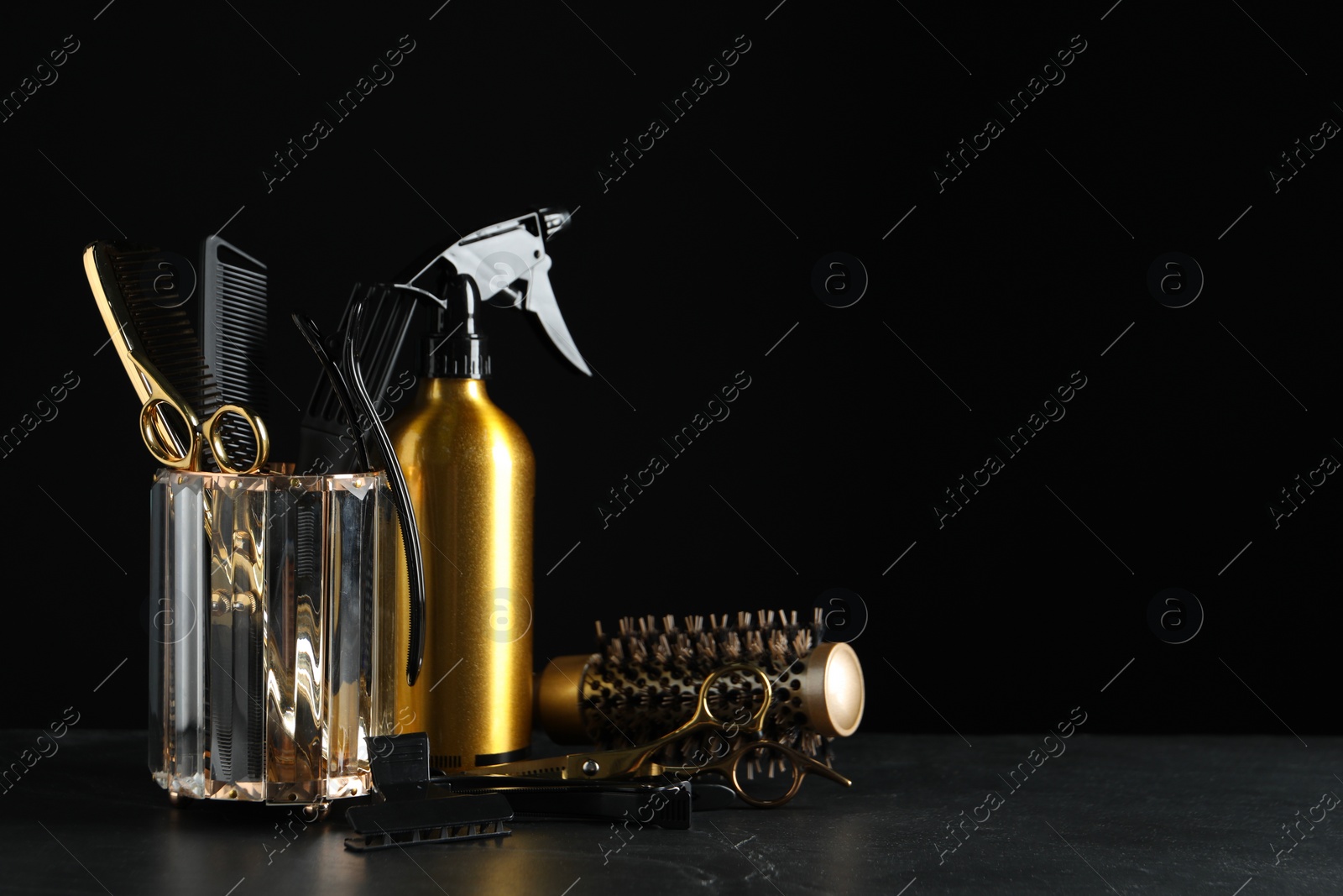 Photo of Different hairdresser tools on grey table against black background. Space for text